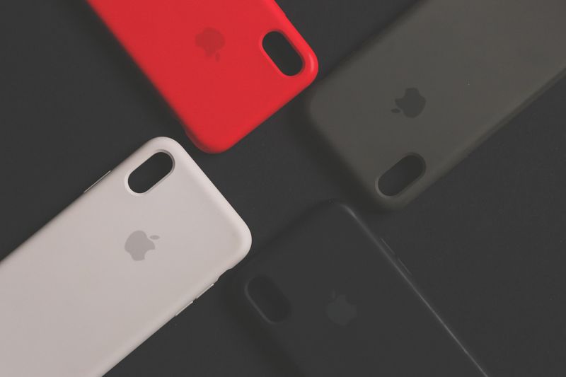 Person designing a custom phone case on a laptop with phone cases and color swatches spread across a desk